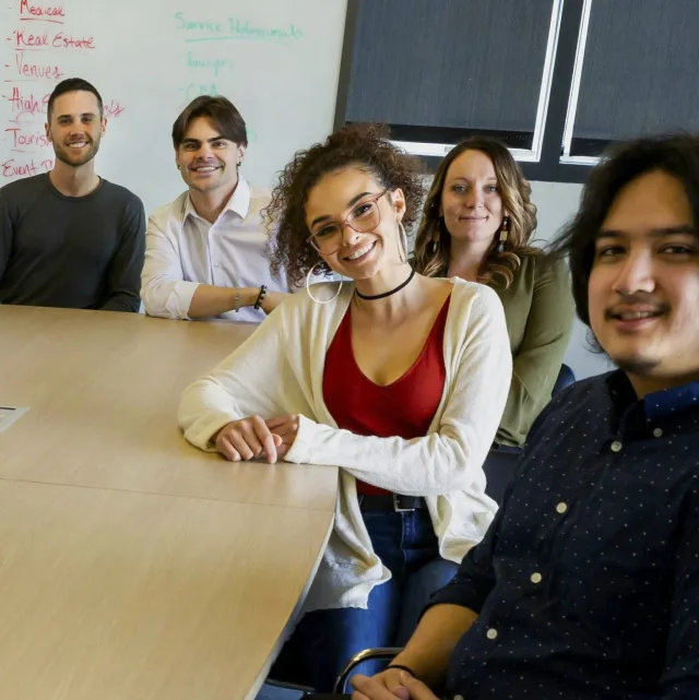 Cinq collègues réunis autour d'une table de réunion, souriants, dans une salle d'entreprise